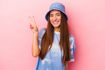 Young caucasian woman isolated on pink background joyful and carefree showing a peace symbol with fingers.