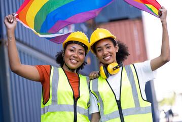 Two young foreman beautiful smiling girls with LGBT flag at container site