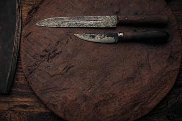 two vintage knives on an old wooden round cutting board near a cleaver blade