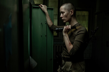 Side view portrait of tough young woman searching lockers with flashlight in dark industrial room,...