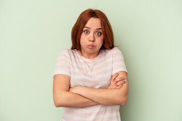 Young caucasian woman isolated on green background blows cheeks, has tired expression. Facial expression concept.