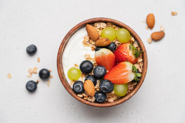 Greek yogurt with berries and granola in wooden bowl. Healthy breakfast with strawberries, grapes, blueberries, oatmeal and almonds