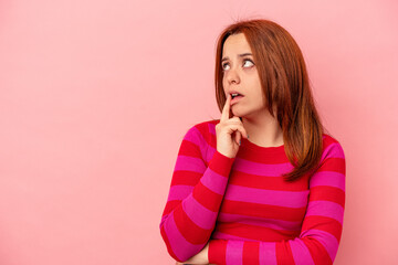 Young caucasian woman isolated on pink background looking sideways with doubtful and skeptical expression.