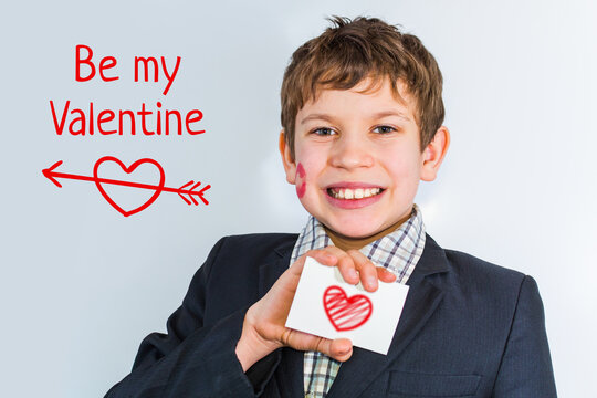 A teenage boy holds a card with a heart in his hand. The boy imprinted lipstick on his cheek.