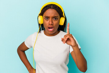 Young African American woman listening to music isolated on blue background  having an idea, inspiration concept.
