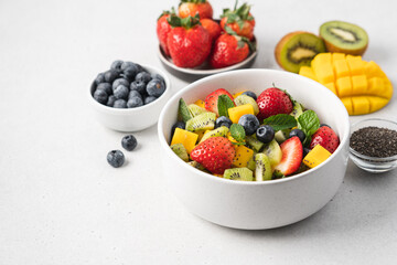 Pieces of mango, strawberries, blueberries, kiwi and mint in white bowl. Fruity fresh raw summer salad