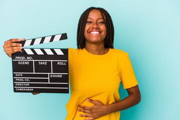 Young african american woman holding a clapperboard isolated on blue background  laughing and...