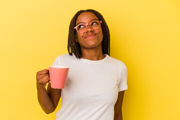 Young african american woman holding a mug isolated on yellow background  dreaming of achieving goals and purposes