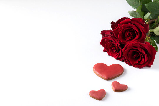 Red roses and gingerbread hearts on a white background with blank space on the left