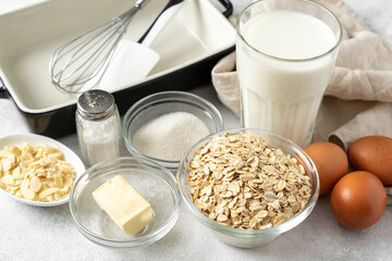 Ingredients for pudding or oatmeal pie on a light gray culinary background. Eggs, cereals, almonds, sugar, milk and butter on the kitchen table
