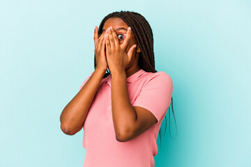 Young african american woman isolated on blue background  blink through fingers frightened and nervous.