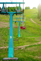 Fototapeta na wymiar Chairlift at the ski resort, view from below. Elevator in the summer season. Moving rope and chairs. Green pine forest in the mountains.