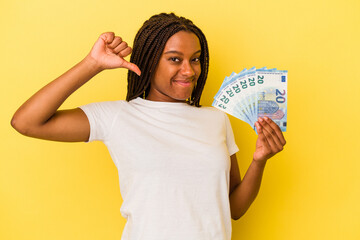 Young african American woman holding bills isolated on yellow background  feels proud and self confident, example to follow.