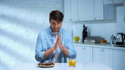 Fototapeta na wymiar pleased man rubbing hands near toasts with confiture and orange juice in kitchen