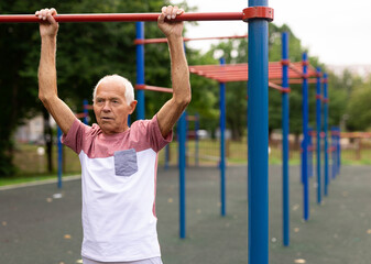 Elderly man hanging from pullup bar and doing pull-ups