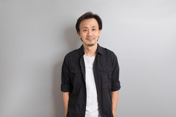 Middle age Asian man in black shirt smile on grey background.