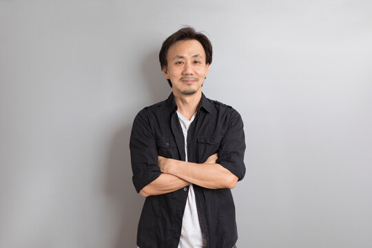 Middle age Asian man in black shirt smile on grey background.