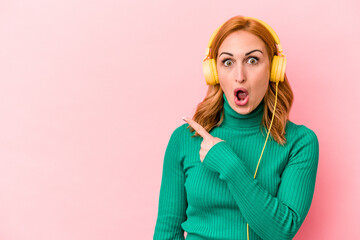 Young caucasian woman listening to music isolated on pink background pointing to the side