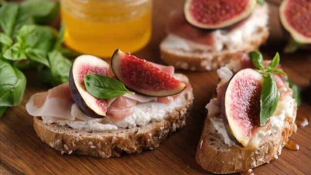 Toast with ricotta, figs and prosciutto served with natural flower honey. Gourmet snack or appetizer. Honey pouring