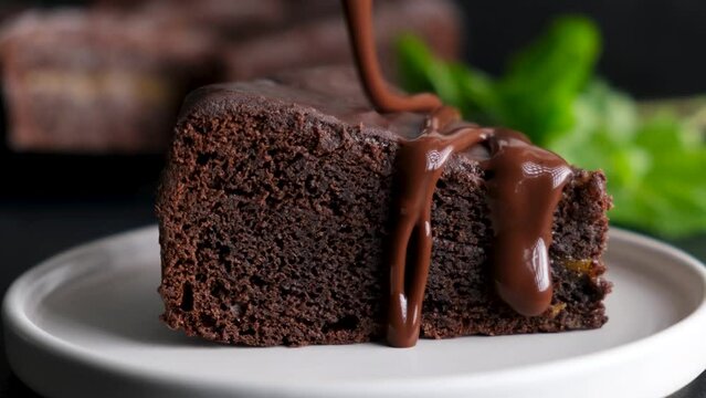 Pouring chocolate glaze on slice of chocolate cake. Delicious brownie cake closeup view