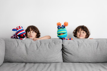 Funny twin brothers making puppet show behind couch