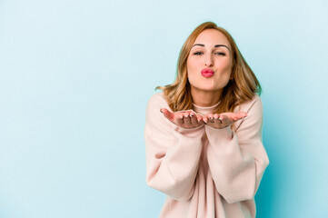 Young caucasian woman isolated on blue background folding lips and holding palms to send air kiss.