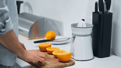 cropped view of man near halves of fresh oranges and electric juicer in kitchen