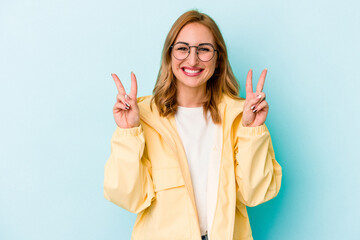 Young caucasian woman isolated on blue background showing victory sign and smiling broadly.