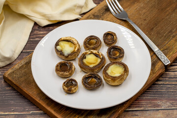 Baked mushrooms in a ceramic plate on a wooden background. Cultivated mushroom or portabello mushroom