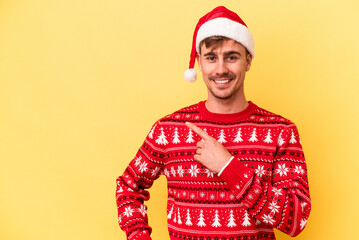 Young caucasian man celebrating Christmas isolated on yellow background smiling and pointing aside, showing something at blank space.
