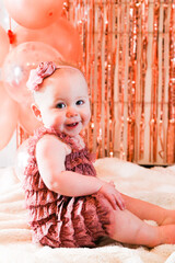 Cute birthday girl celebrating her one year birthday by messily eating a cake surrounded by pink background streamers and balloons
