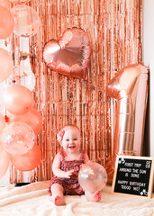 Cute birthday girl celebrating her one year birthday by messily eating a cake surrounded by pink background streamers and balloons
