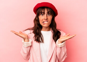 Young Argentinian woman isolated on pink background confused and doubtful shrugging shoulders to...