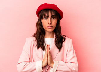 Young Argentinian woman isolated on pink background praying, showing devotion, religious person looking for divine inspiration.