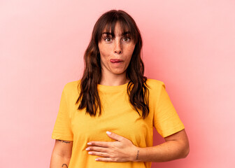 Young Argentinian woman isolated on pink background touches tummy, smiles gently, eating and satisfaction concept.