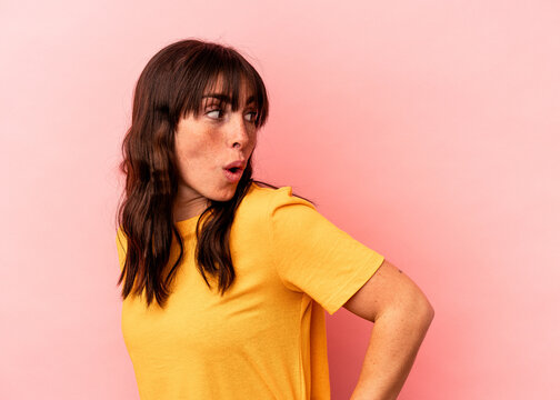 Young Argentinian woman isolated on pink background looks aside smiling, cheerful and pleasant.