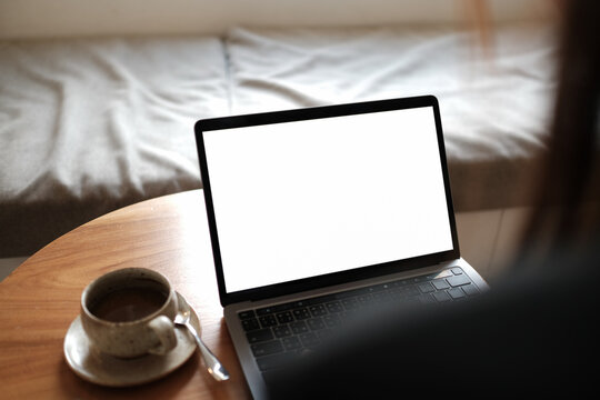 Mockup image of a businesswoman using laptop with blank white desktop screen with coffee cup on wooden table in cafe..