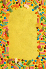 Fototapeta na wymiar Colorful assortment of candies in shape of frame on yellow background. Top view, copy space