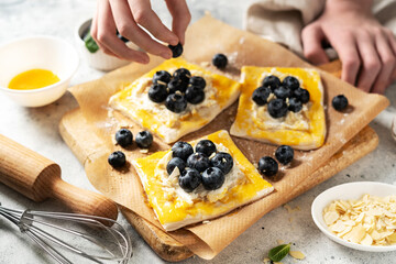 Raw puff pastry with cheese cream and blueberries. The process of making delicious sweet buns or mini pies	