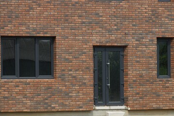 the wall of a private brown brick house with a black plastic glazed door and a two windows on the...