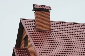 one large red brick chimney on the tiled roof of a private house against a gray sky