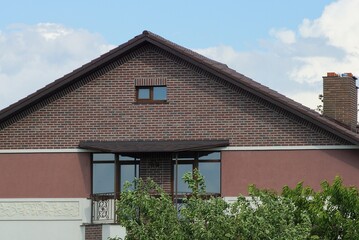 brown brick attic of a private house with an iron balcony with windows on the street against a blue sky