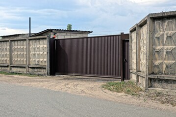 Fototapeta premium one closed brown metal gate and part of a gray concrete wall fence on the street