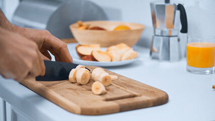 cropped view of man cutting fresh banana on chopping board in kitchen