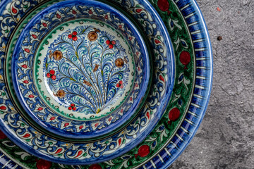 Three hand painted blue ceramic dishes, traditional Uzbek utensils dishes, bowl, plates with national floral ornament on dark background, Long banner format. top view