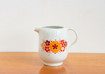 Mid-century modern porcelain milk jug with orange flower pattern - on a wooden table isolated