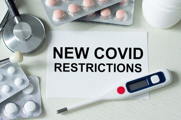 text new covid restrictions on the card on the table next to the thermometer, stethoscope and tablets, medical concept