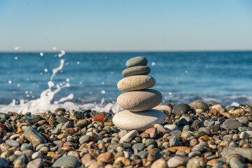 Fototapeta na wymiar Beautiful pyramid of pebbles on the seashore with splashing waves on a sunny day, copy the space. Concept of balance, harmony