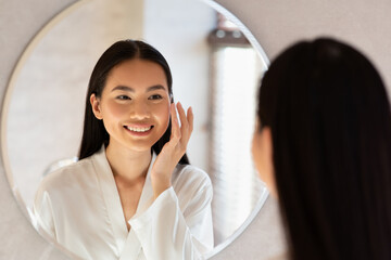 Happy beautiful korean lady using moisturising face cream