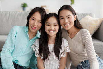 Obraz premium Positive multi generation Asian family posing and smiling at camera, sitting on floor in living room